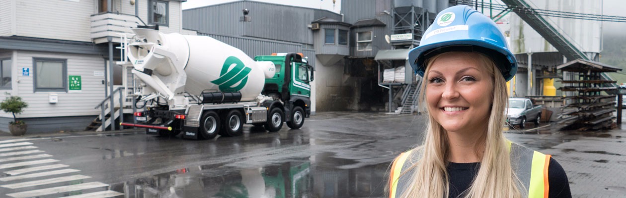 Smilende jente står forann siloer i Ølen Betong